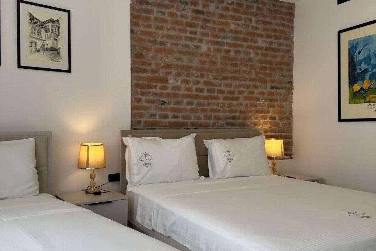 A hotel room with a brick accent wall, two beds with white linens, and two bedside lamps.