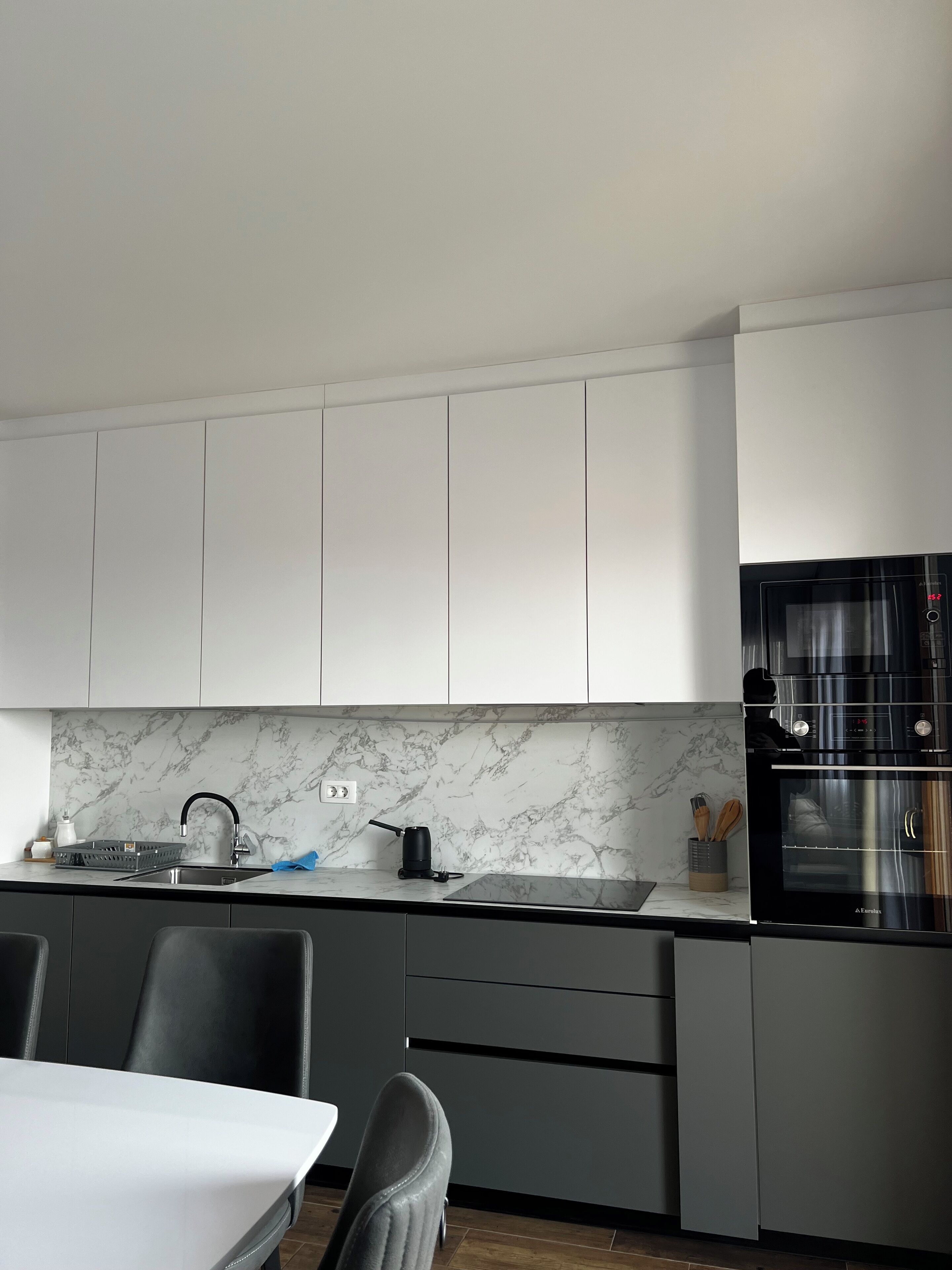 Una cucina moderna con mobili grigi, una schiena di marmo, un piano cottura nero e un forno integrato.