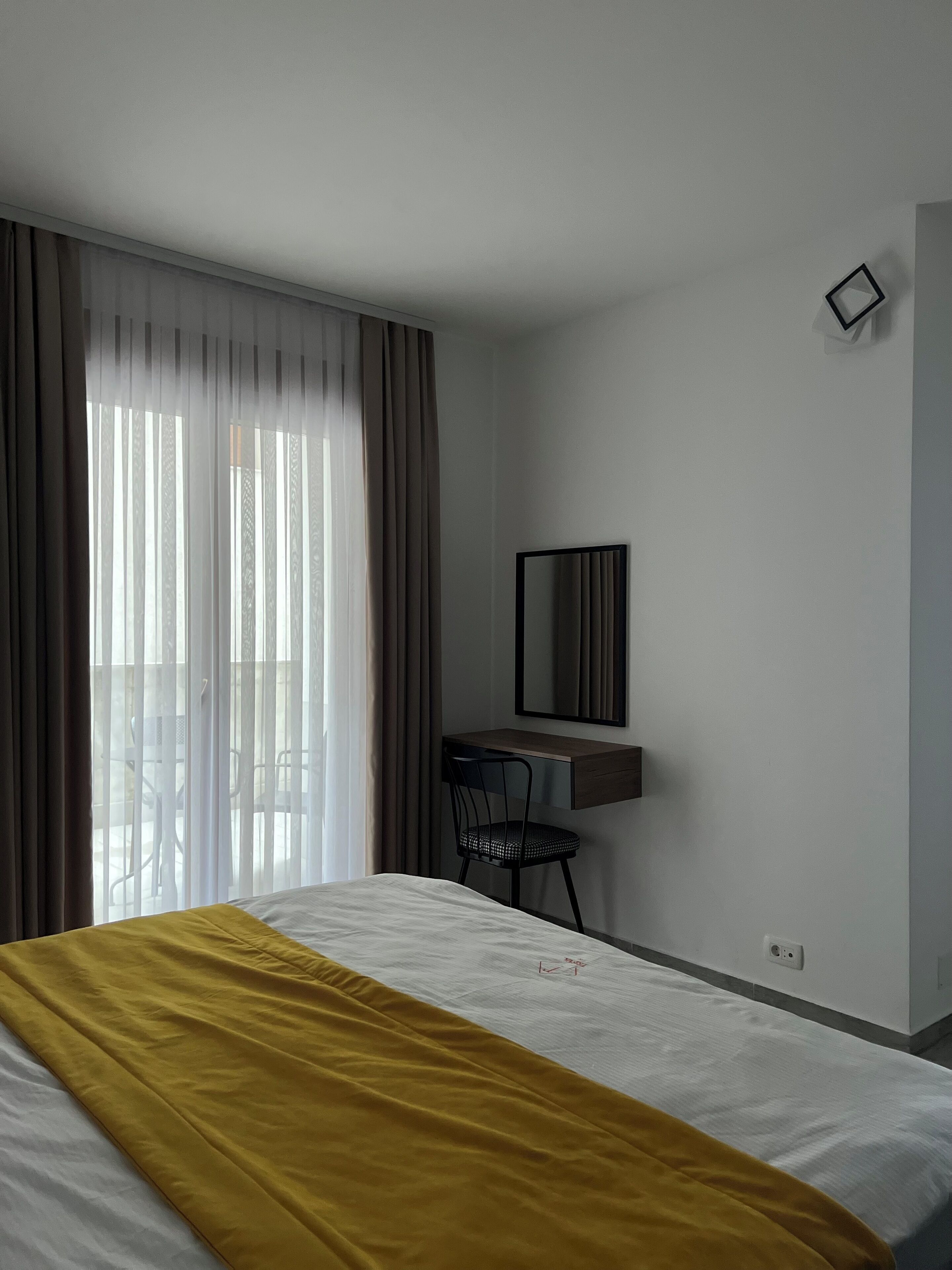 Una habitación de hotel con cama, escritorio, silla, espejo y ventana con cortinas.