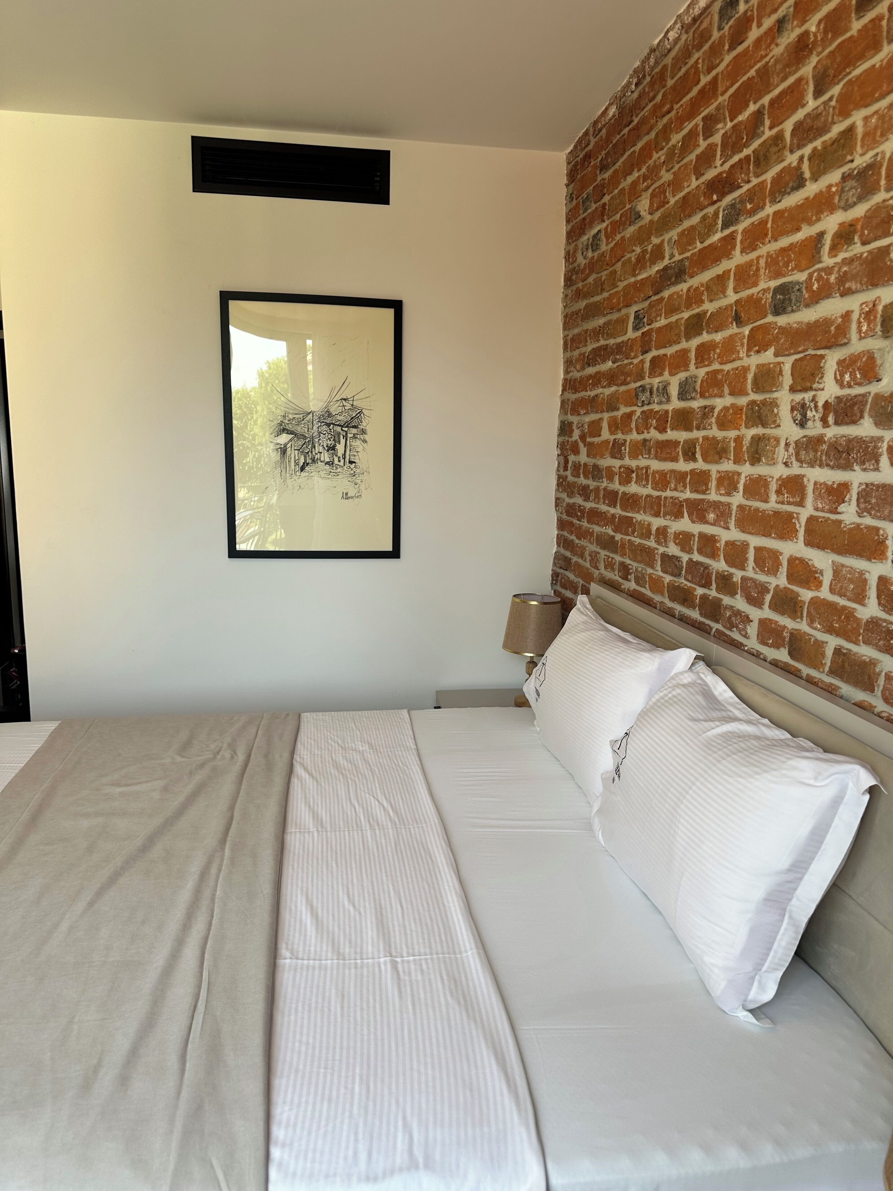 Una camera da letto con un letto grande, un muro in mattoni, un quadro incorniciato e una lampada da comodino.