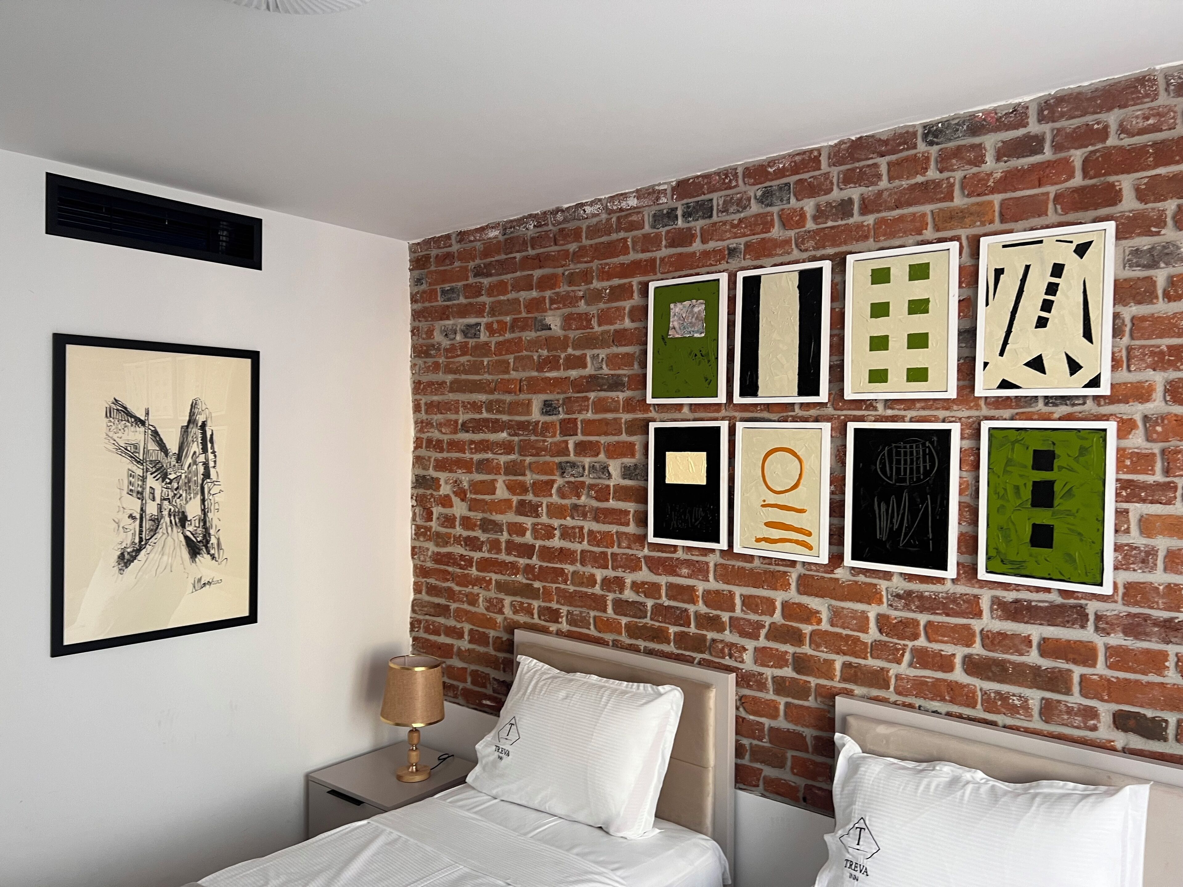 A hotel room with a brick wall, a bed with white bedding, a nightstand with a lamp, and a framed picture on the wall.