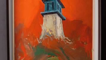 Un tableau encadré représentant un phare perché sur une falaise, avec un fond orange.