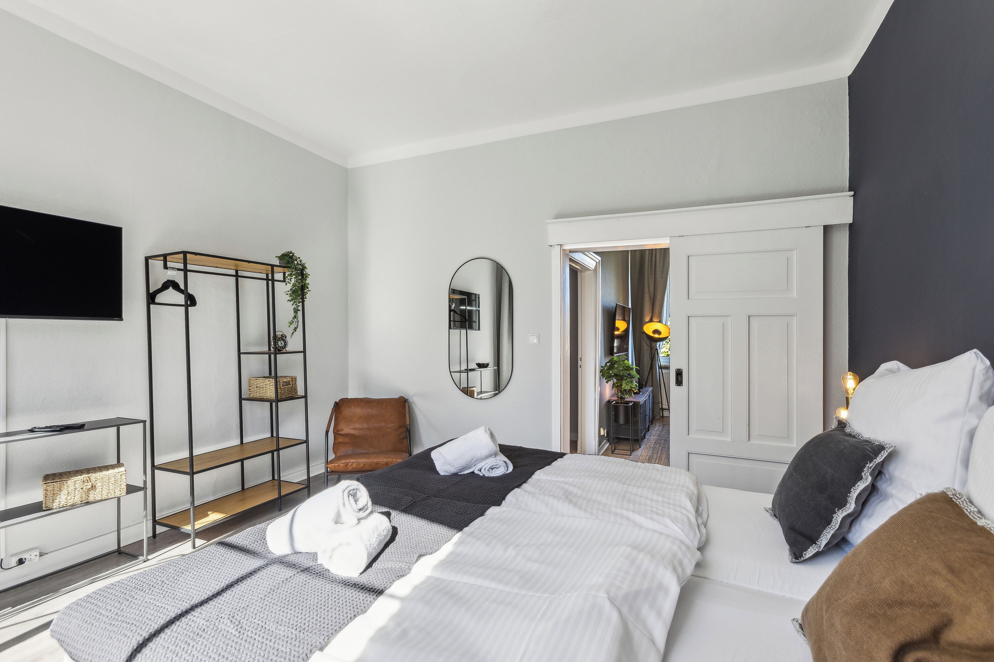 Une chambre d’hôtel moderne équipée d’un lit, d’une télévision, d’un coin salon avec un fauteuil et d’un miroir.