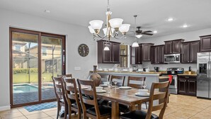 A spacious kitchen with dark wooden cabinets, a stainless steel refrigerator, and a dining area with a large wooden table and chairs. - Disney! Private Pool, Hot Tub, Game Room & Themed Bedrooms. Book Now! #CG3504 (Orlando)