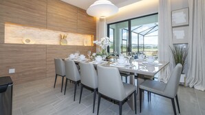 Un'area pranzo moderna con un tavolo lungo apparecchiato per sei persone, circondato da sedie. La stanza presenta una parete d'accento in legno, un'ampia finestra con vista e una lampada a sospensione sopra il tavolo.
