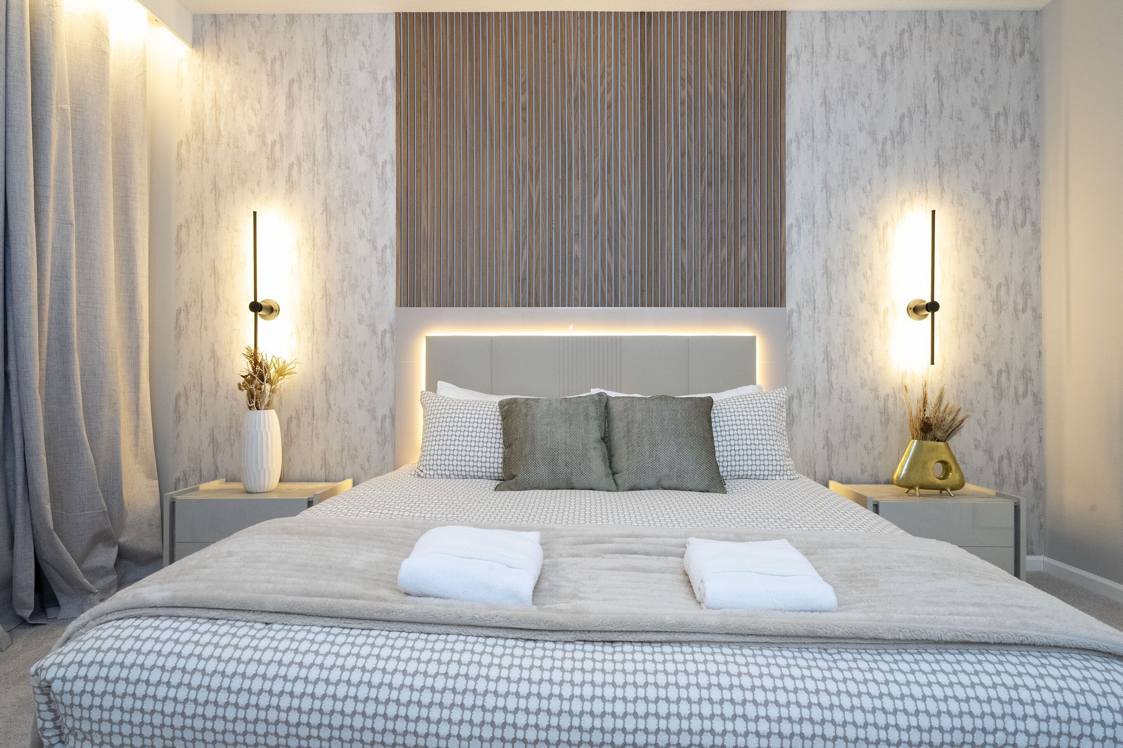 A modern hotel room with a large bed, two bedside tables, and a headboard with vertical lines.