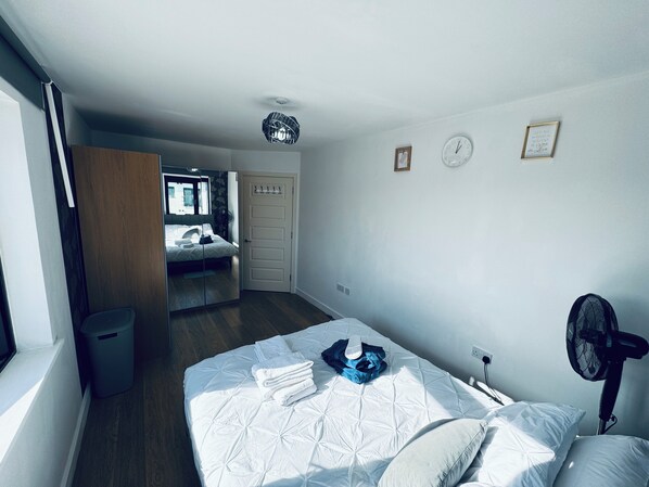 A bedroom with a bed, a mirror, a door, and a wall clock.
