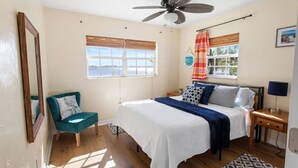 A bedroom with a bed, a chair, a nightstand, a lamp, a ceiling fan, and a window with a view. - LakeFront Sunrise Cottage (Sebring)