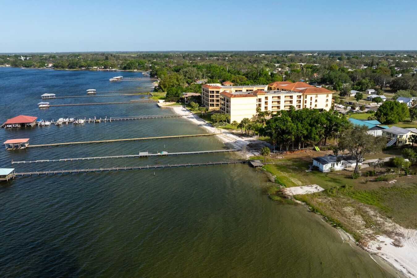 A coastal hotel with multiple buildings, a dock with boats, and a sandy beach.