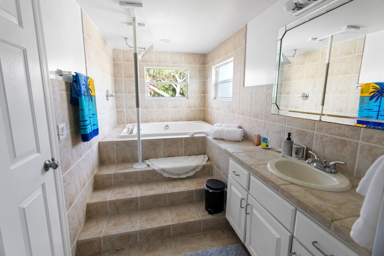 A bathroom with a bathtub, a sink, and a shower. There are steps leading to the bathtub, and a window providing natural light.