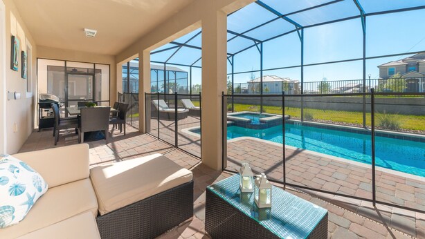 A covered patio with a pool, wicker furniture, and a glass table.