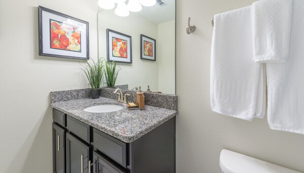 Un baño con encimera de granito, lavabo, espejo y toallero.