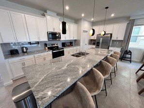 A modern kitchen with white cabinets, a granite countertop, and a central island with bar stools. - Last Minute Disney! Private Pool, Hot Tub, Game Room & Themed Bedrooms. Book Now! #115435 (Orlando)