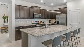 A modern kitchen with dark cabinets, a granite island, bar stools, and stainless steel appliances. - Last Minute Disney Getaway! Private Pool & Themed Bedrooms. Book Now! #66193 (Orlando)