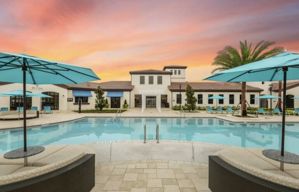 A hotel pool area with a sunset view, lounge chairs, and umbrellas.