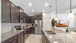 A modern kitchen with dark cabinets, stainless steel appliances, granite countertops, and pendant lighting. - Last Minute Disney Getaway! Private Pool & Themed Bedrooms. Book Now! #65821 (Orlando)