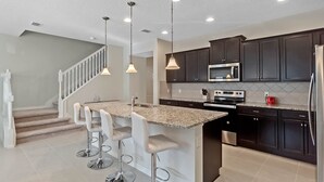 A modern kitchen with dark cabinets, a stainless steel refrigerator, a microwave, and a granite countertop island with bar stools. - Last Minute Disney Getaway! Private Pool & Themed Bedrooms. Book Now! #65821 (Orlando)