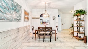 A dining area with a wooden table and chairs, a chandelier, and a large floral painting on the wall.