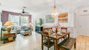 A spacious living room with a sofa, a dining table set for four, and a ceiling fan.