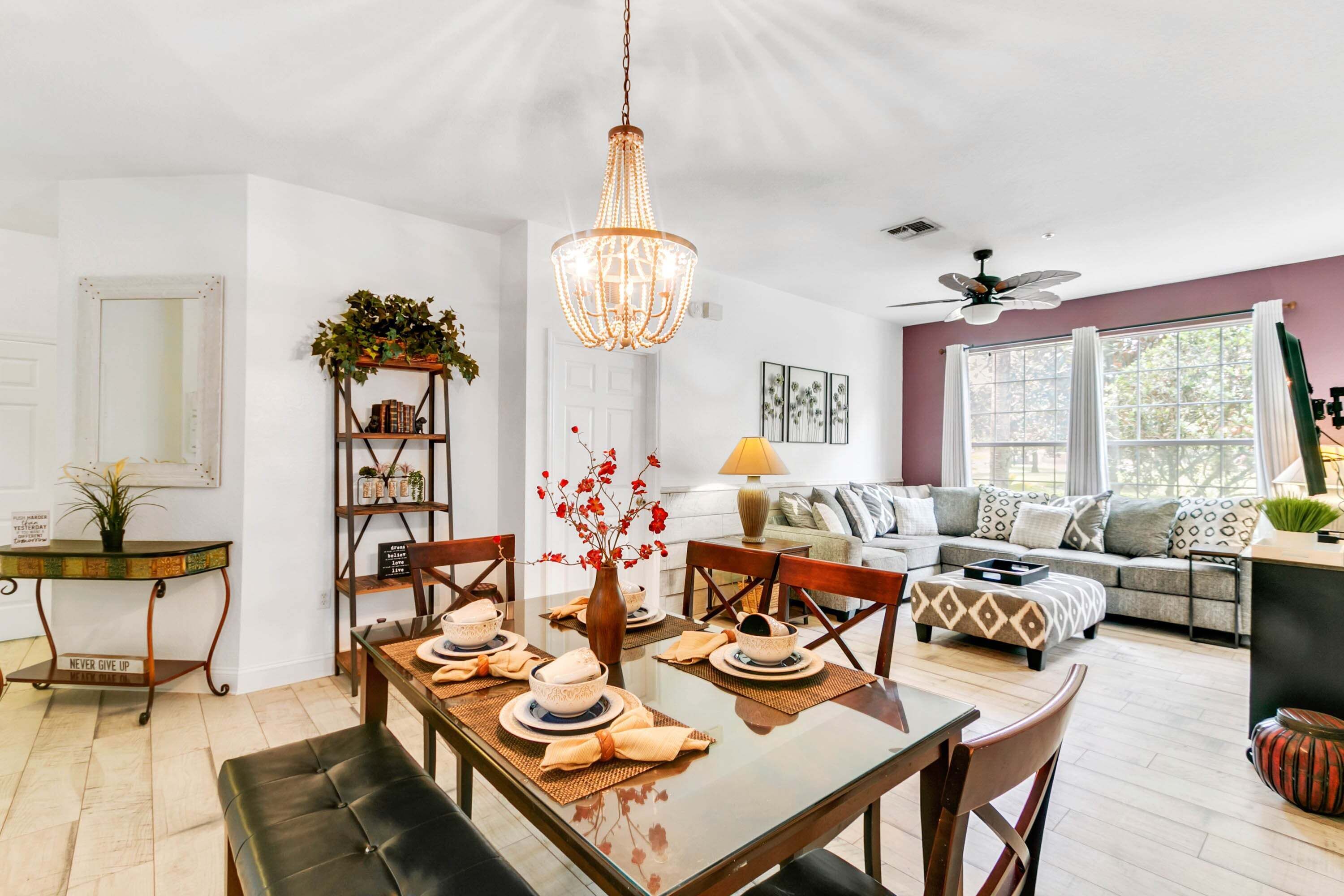 A dining area with a wooden table set for four, a chandelier, and a bookshelf with decorative items.