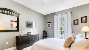 A bedroom with a bed, a dresser, a TV, and a window with curtains.