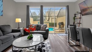 A modern living room with a sofa, coffee table, and chairs. There is a pool visible through the glass doors. - Last Minute Disney Getaway! Private Pool & Themed Bedrooms. Book Now! #66159 (Orlando)