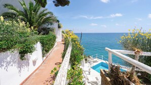 A coastal terrace with a pool, white walls, and lush greenery.