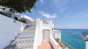 A set of stairs with blue and white patterned tiles leading to a white door, overlooking a body of water.