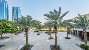 A spacious outdoor area with palm trees and a fountain, surrounded by modern buildings.