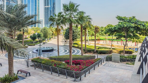 A landscaped urban area with palm trees, a circular water feature, and a playground.