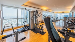 A gym with cardio machines, weight stations, and a large window offering a city view.