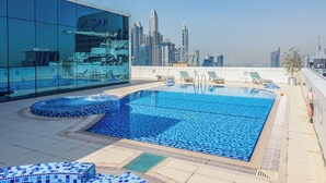 A rooftop pool with lounge chairs, a glass building, and a city skyline in the background.