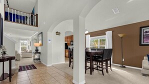 A spacious living area with a dining table, kitchen in the background, and a staircase leading to an upper level. - Last Minute Disney! Private Pool, Game Room & Themed Bedrooms. Book Now! #65689 (Orlando)
