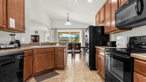 A kitchen with wooden cabinets, a black refrigerator, a microwave, a stove, and a dishwasher. - Last Minute Disney! Private Pool, Game Room & Themed Bedrooms. Book Now! #65689 (Orlando)