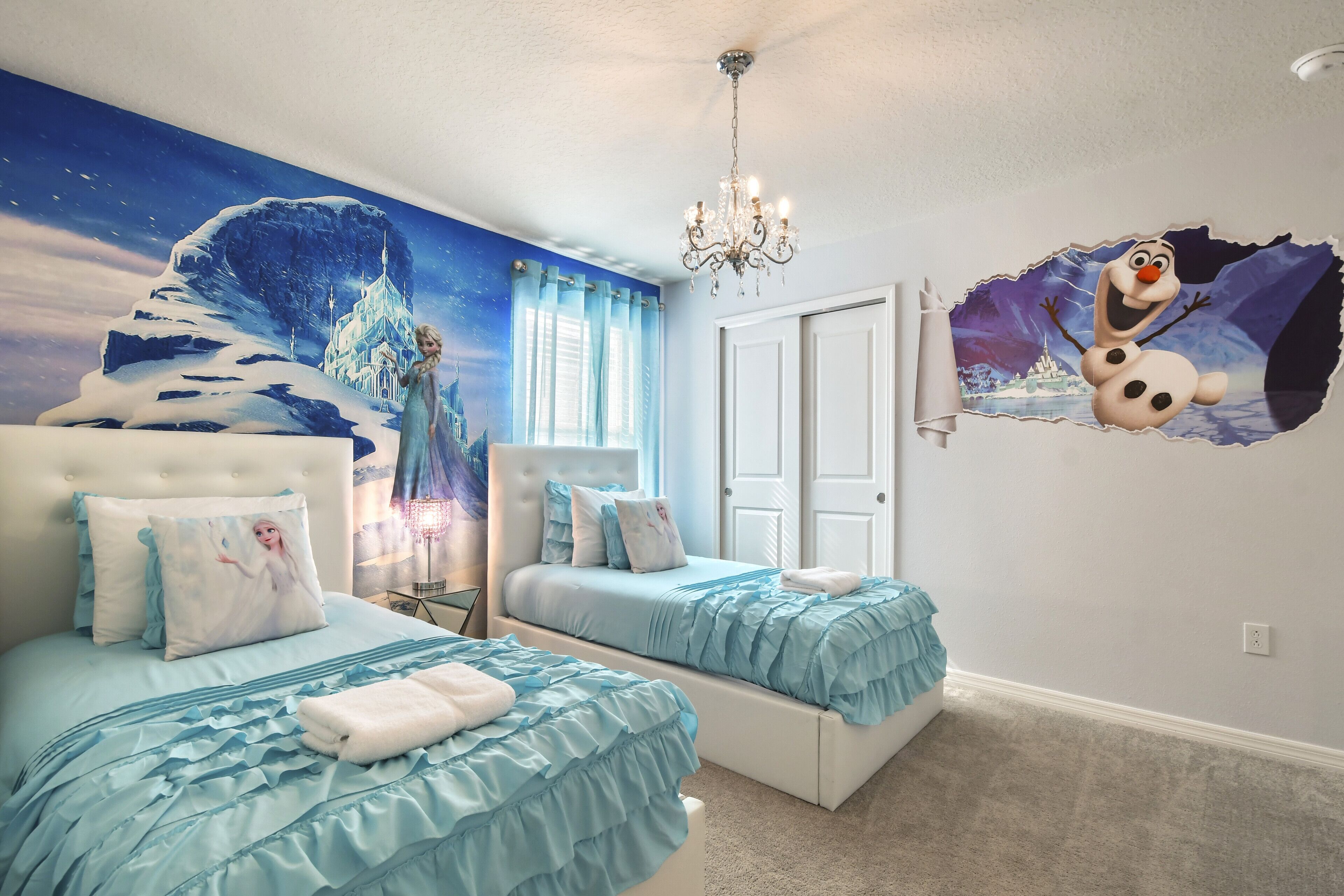 A bedroom with two beds, a chandelier, a mural, and a wall decal.