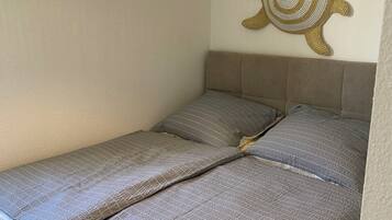 Un letto con una coperta grigia e cuscini, un arazzo e una lampada di vimini.