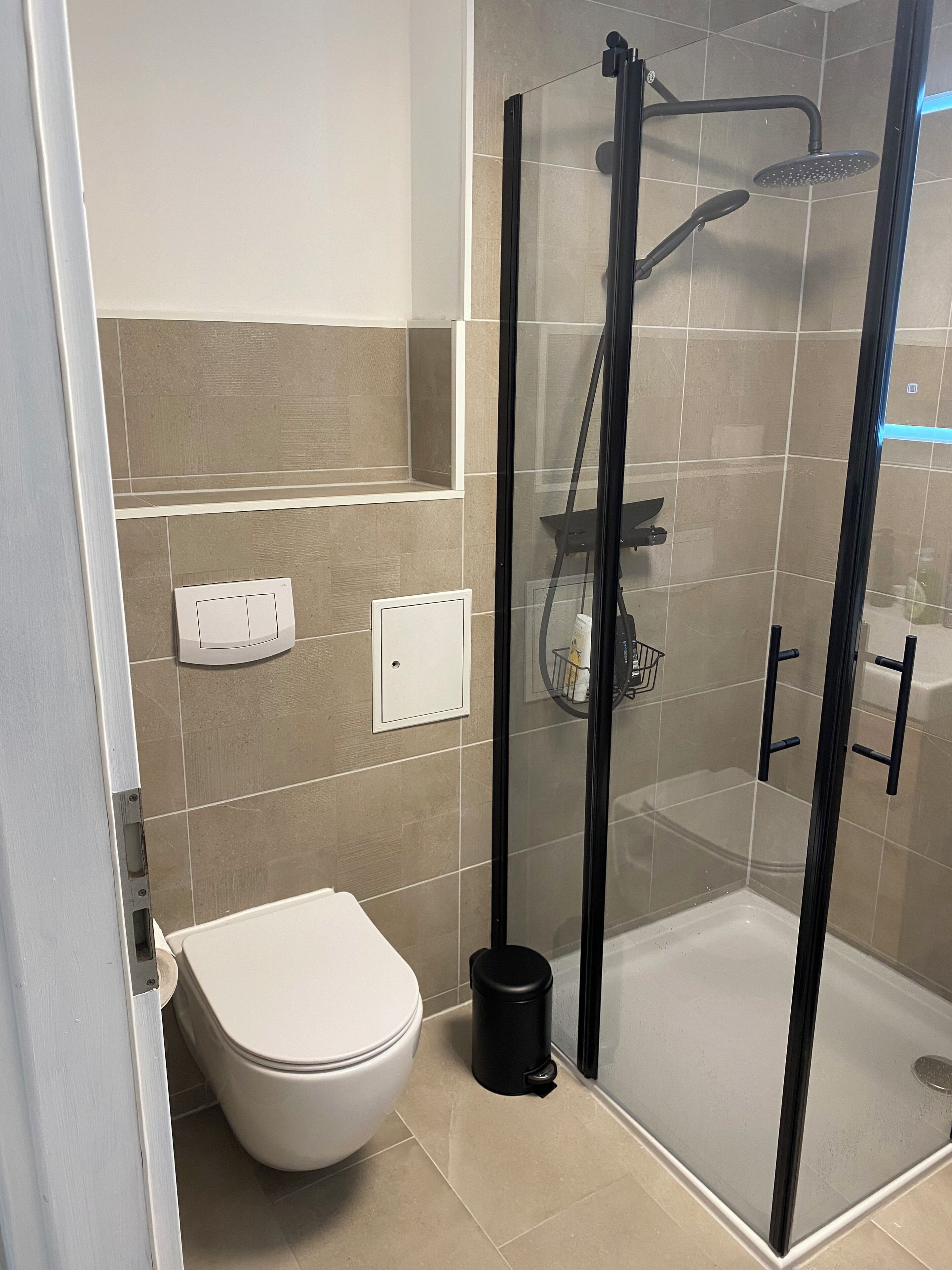 Un bagno moderno con doccia vetro-ceramica, un water e un cestino.