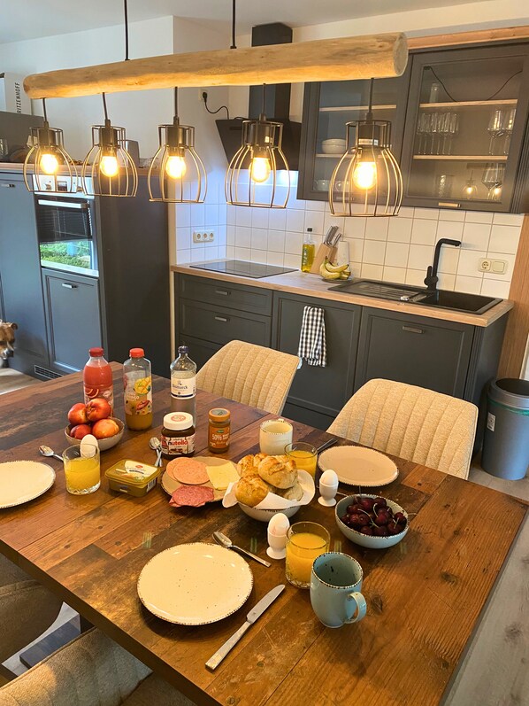 A modern kitchen with a wooden dining table set for breakfast, featuring a variety of foods and drinks.