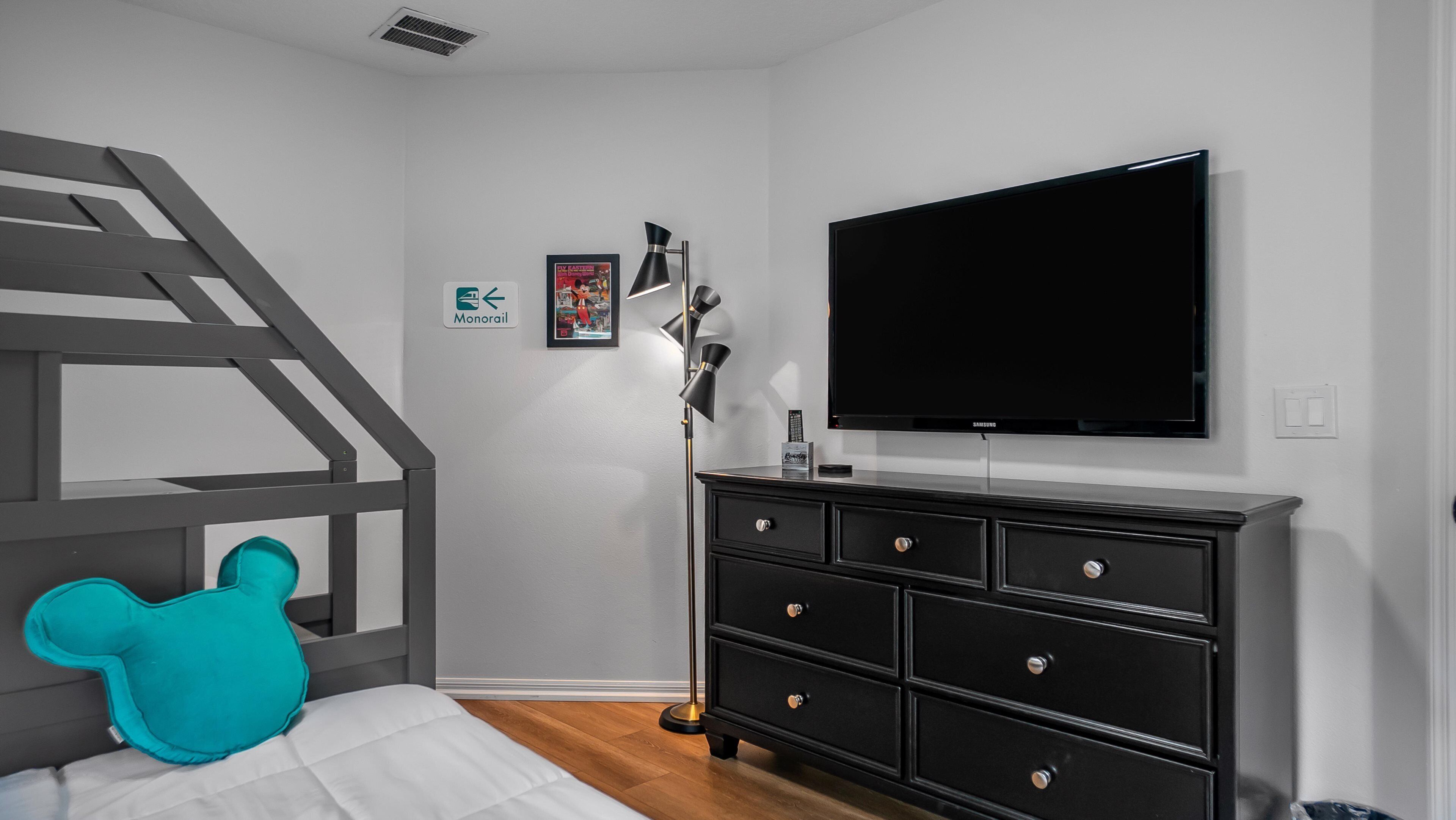 Un dormitorio con cama, cómoda, televisor, escalera y un cuadro colgado en la pared.