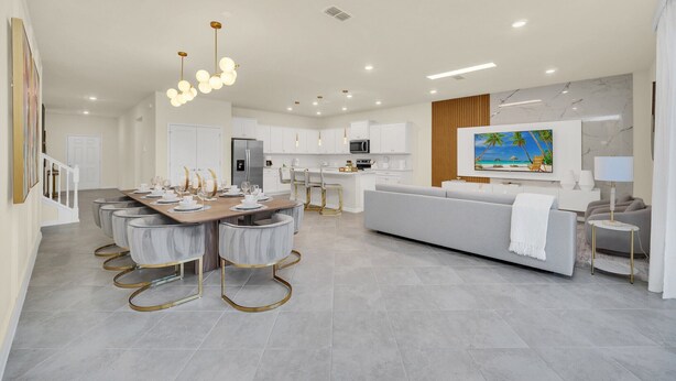 A modern kitchen with white cabinets, a dining area with a long table and chairs, and a living area with a sofa and TV.