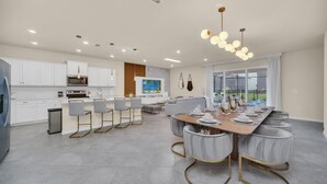 A modern kitchen with white cabinets, a central island, and a dining area with a long table and chairs.