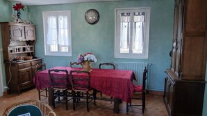 Ein Esszimmer mit Tisch für vier Personen, Holzsesseln, einer Vase mit Blumen, einer Wanduhr und einem Schrank mit Geschirr.