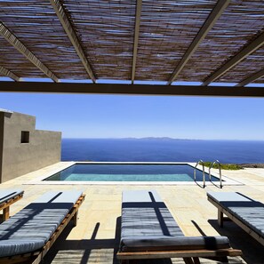An infinity pool with clear blue water, surrounded by lounge chairs and a pergola.