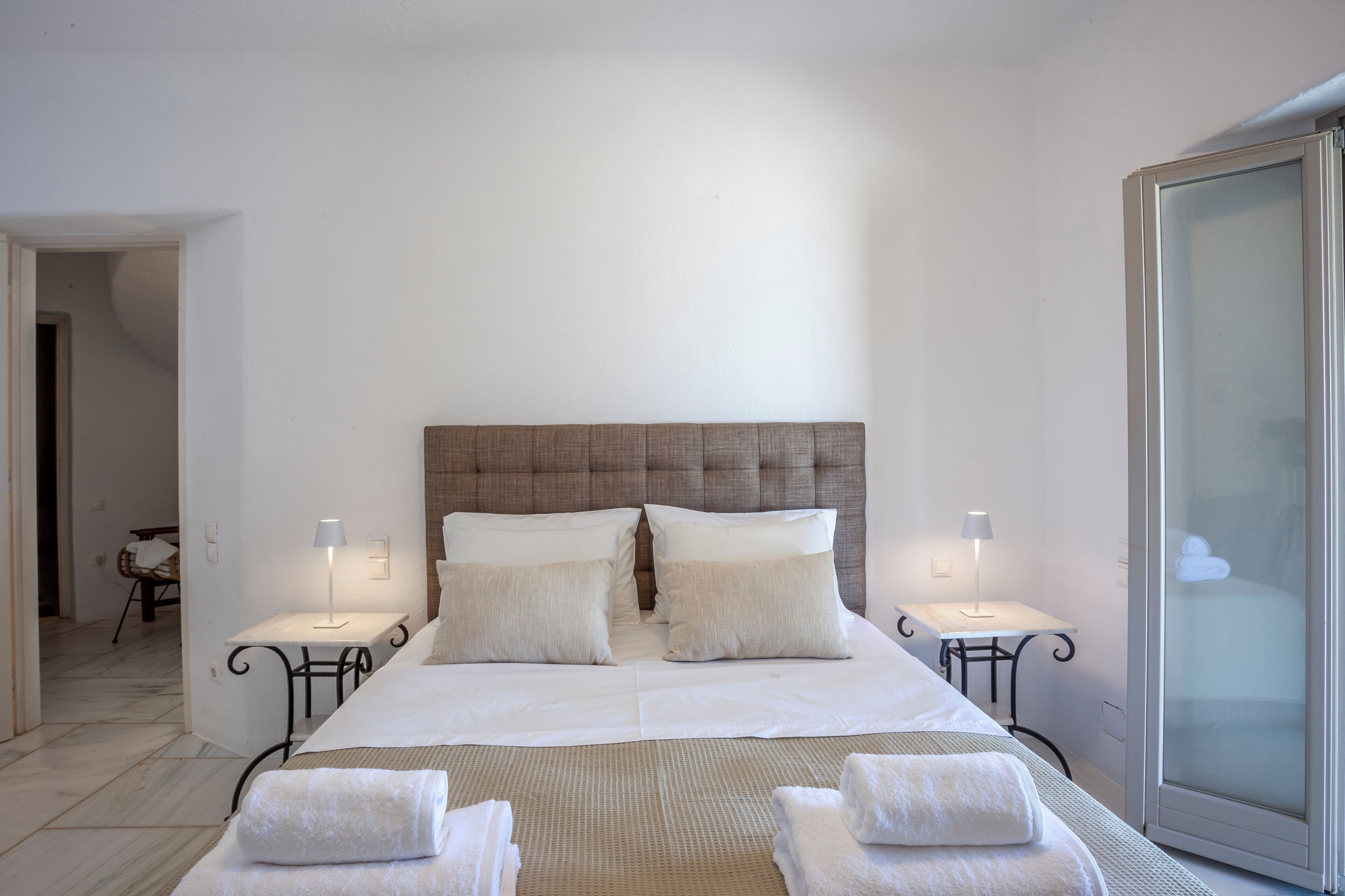 A neatly arranged bedroom with a large bed, two bedside tables with lamps, and a sliding glass door.