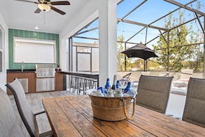 An outdoor kitchen with a grill, bar stools, and a table with a basket of bottled beverages.