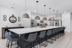 A modern kitchen with a large island, bar stools, pendant lights, and stainless steel appliances.