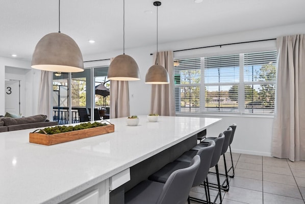 A modern kitchen with a large island, pendant lights, and a view of the outdoors.