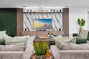 A modern living room with a large flat-screen TV, a marble wall, and a green wall. There are two sofas, a coffee table, and decorative items.