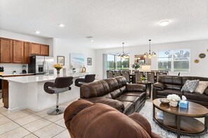 A modern kitchen with a central island, a dining area with a chandelier, and a living room with leather sofas.