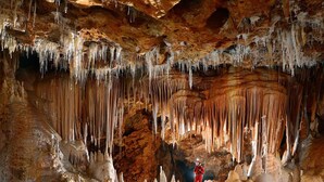 Eine Höhle mit Stalaktiten und Stalagmiten, eine Person in Rot und eine Taschenlampe.
